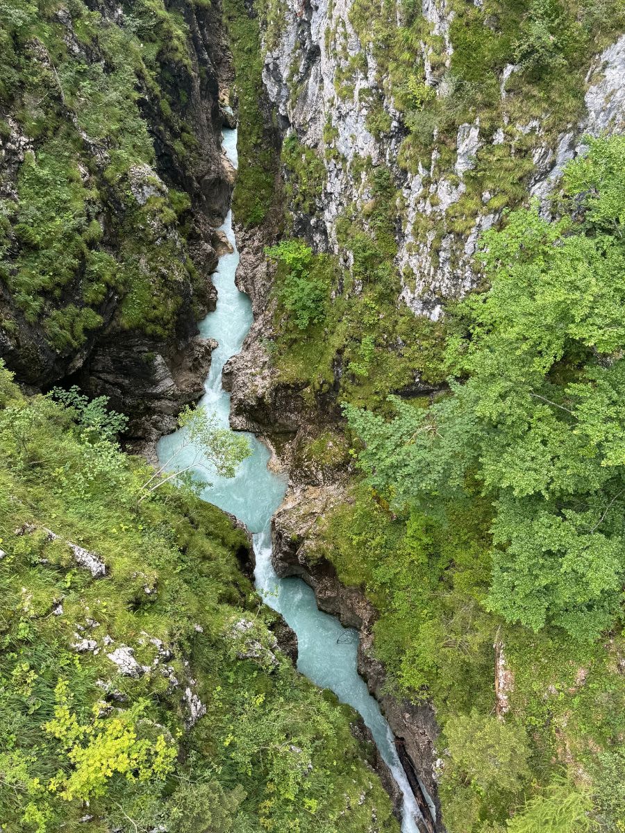 Na dnie wąwozu Leutascher Geisterklamm płynie rzeka Leutascher Ache. Woda jest w kolorze niebieskim. Zbocza wąwozu porasta roślinność.