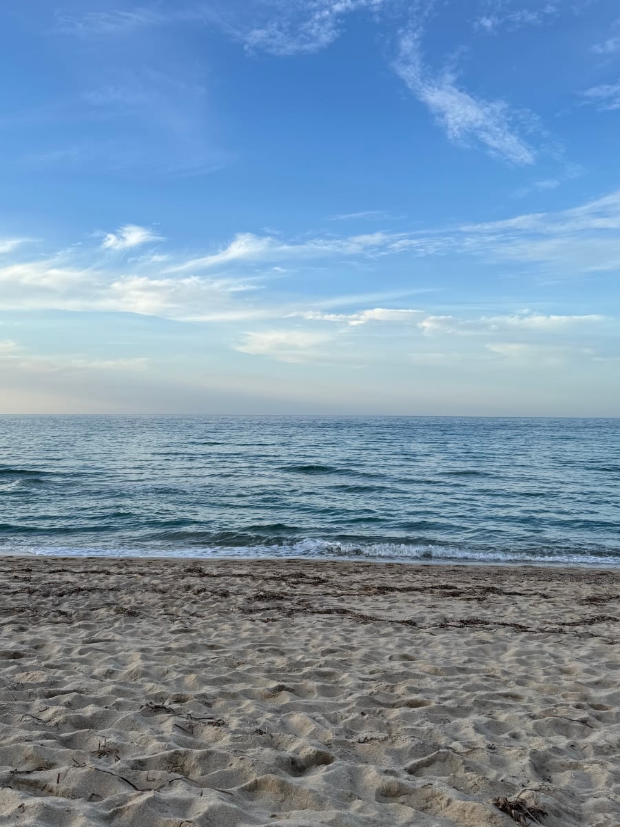 Plaża Spiaggia di Maragnani na Sardynii. Dzień jest pogodny i bezwietrzny, morze spokojne. Na pierwszym planie piasek.