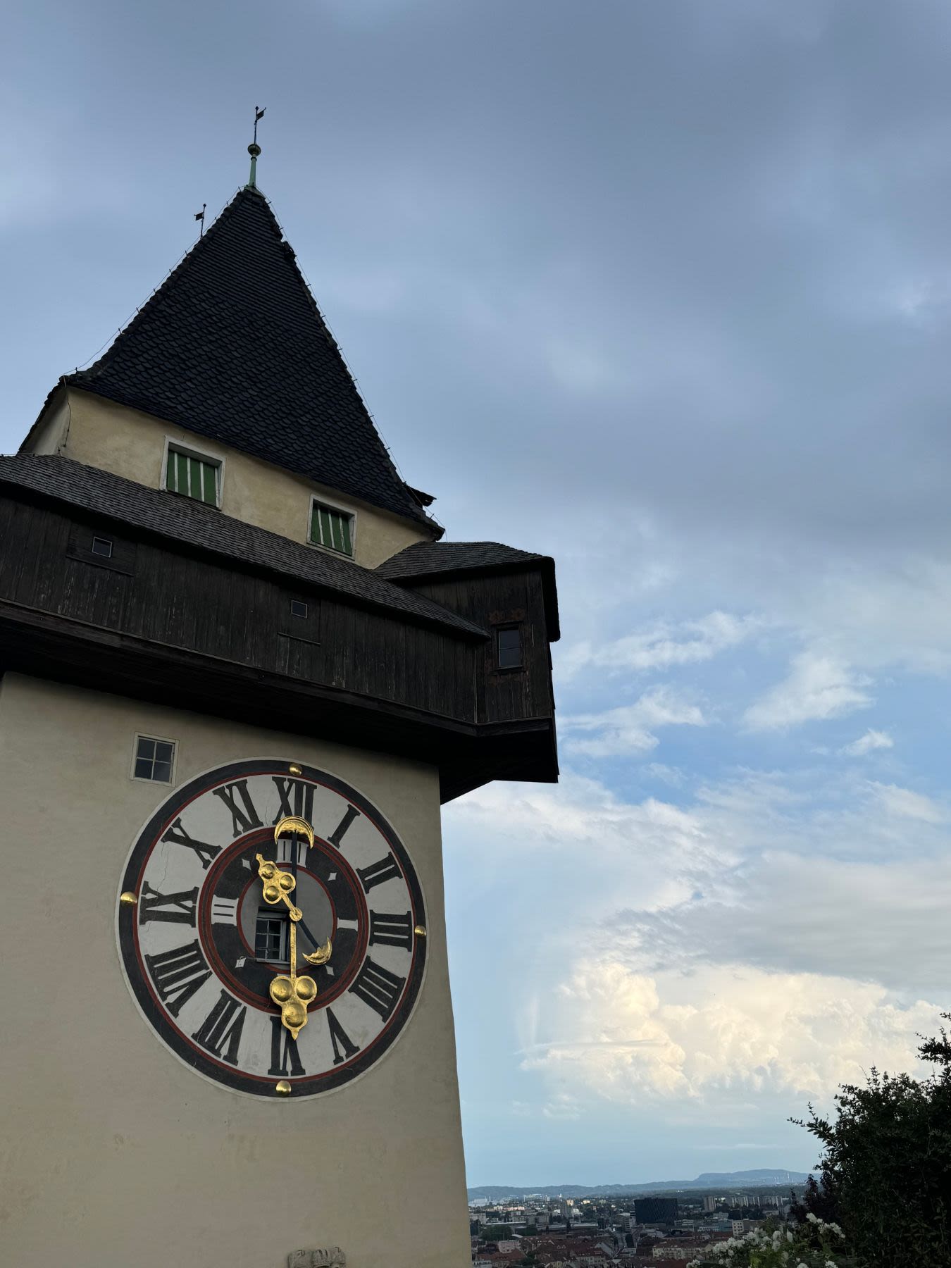 Wieża zegarowa na wzgórzu Schlossberg w Grazu. Na tarczy zegarowej wybijają się złote wskazówki. 
