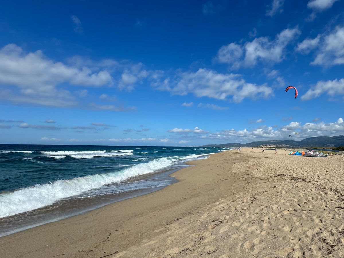 Plaża Spiaggia San Pietro A Mare di Valledoria. Ładna pogoda w październiku. Turyści plażują, niektórzy uprawiają katesurfing.