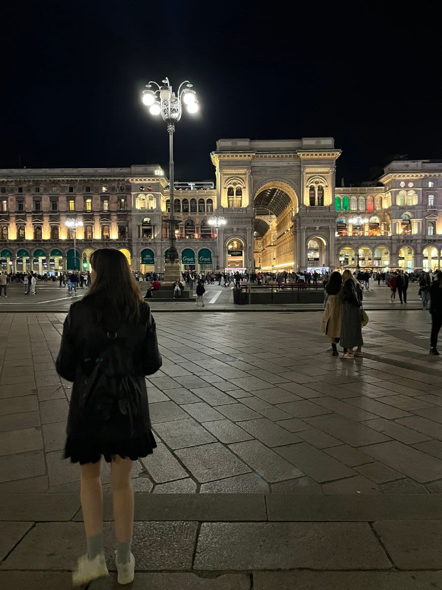 Centrum Mediolanu nocą. Oświetlona Galeria Handlowa Vittorio Emanuele II, przy której chodzą turyści.