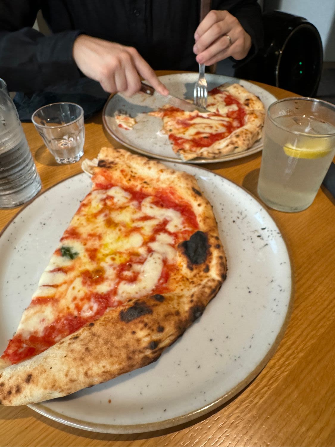 Na dwóch talerzach leżą połówki pizzy Margherita. Mężczyzna kroi pizzę w restauracji Napo Pizza Napoletana w Grazu.