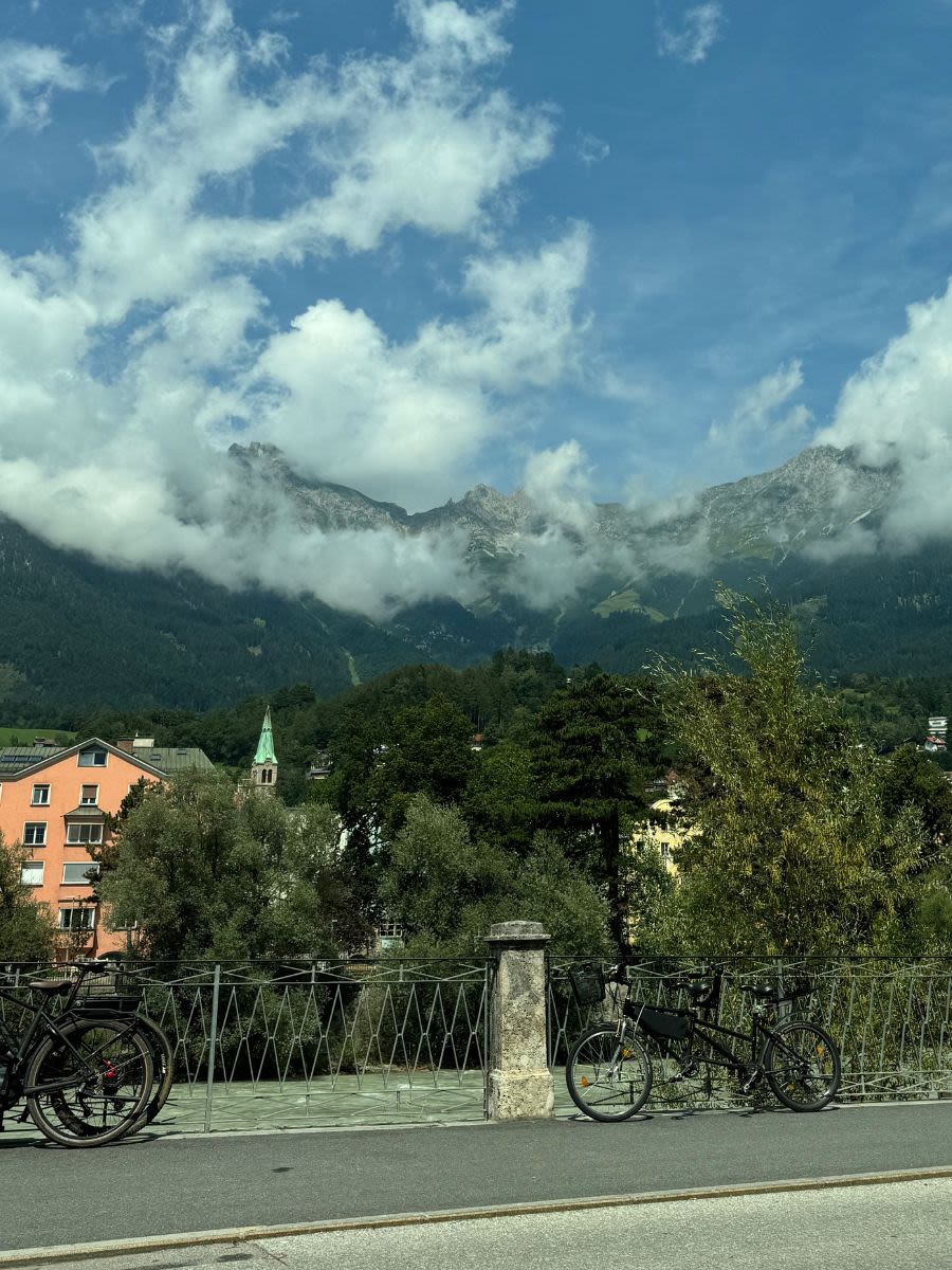 Widok na Innsbruck z samochodu latem. Do balustrad przymocowane są rowery. Jest dużo zieleni, na horyzoncie góry przykryte chmurami.