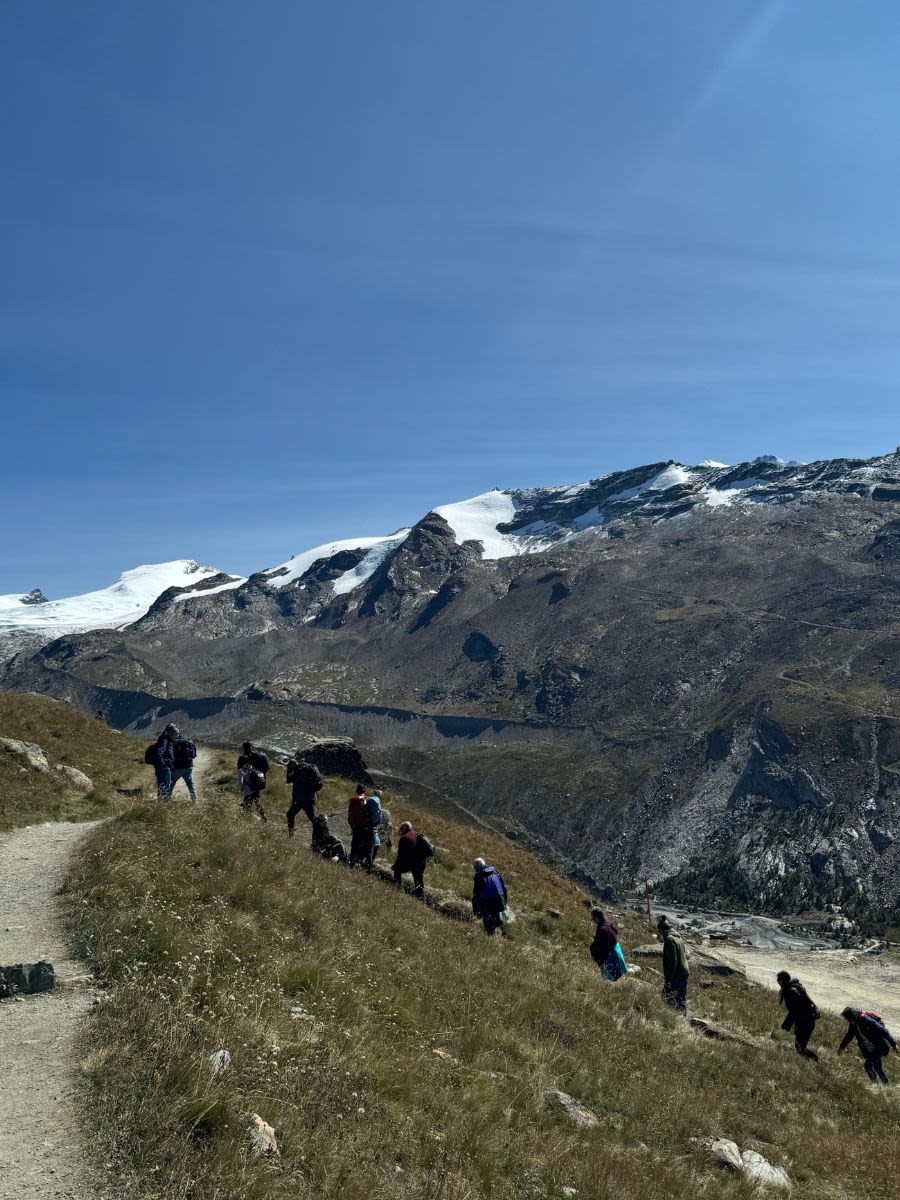 Grupa turystów idzie gęsiego po szlaku pięciu jezior w Szwajcarii. Główną atrakcją szlaku jest widok na Matterhorn.