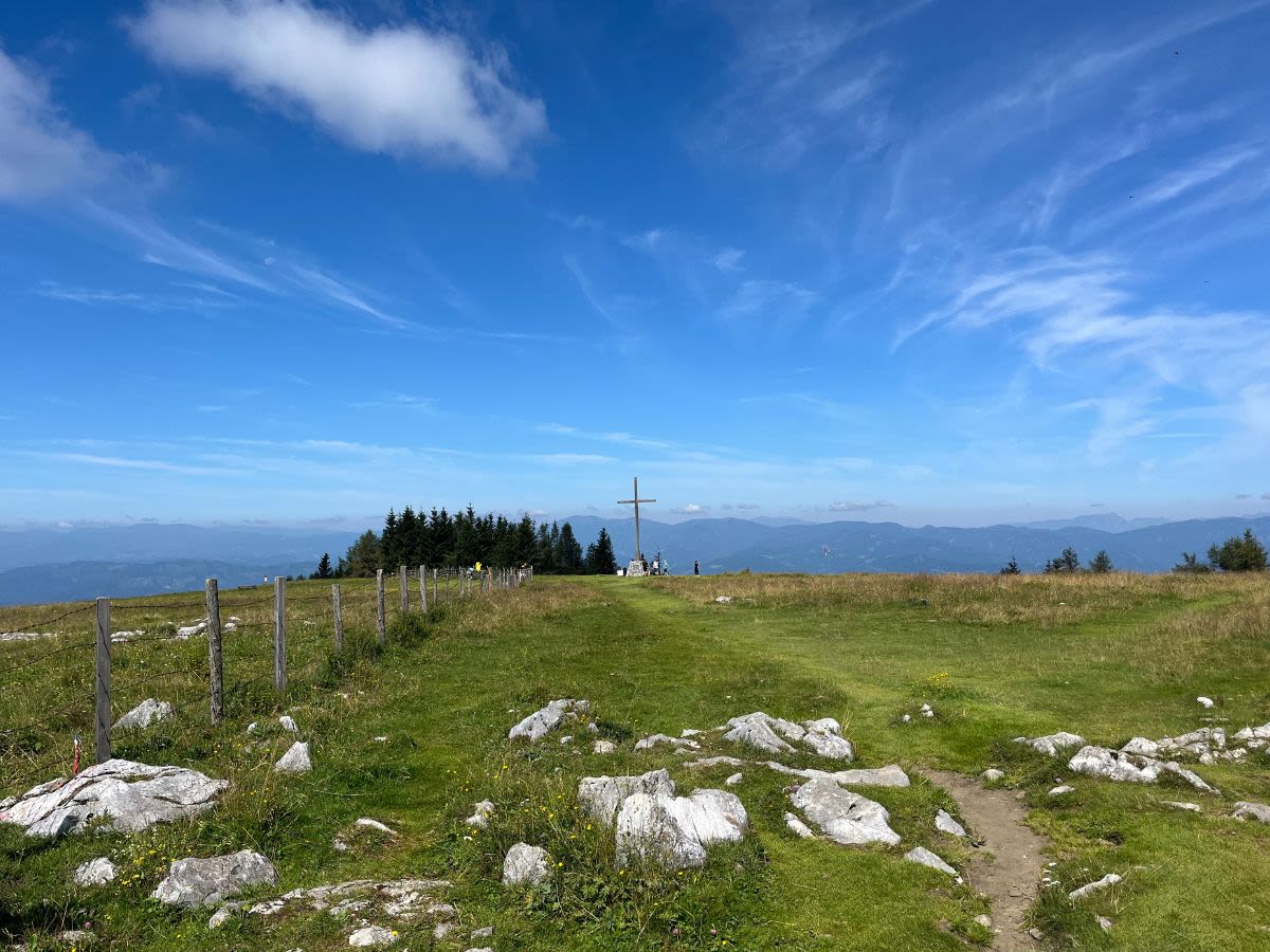 Polana na górze Schöckl w lecie. Po prawej widać drewniane ogrodzenie, na środku w oddali krzyż. 