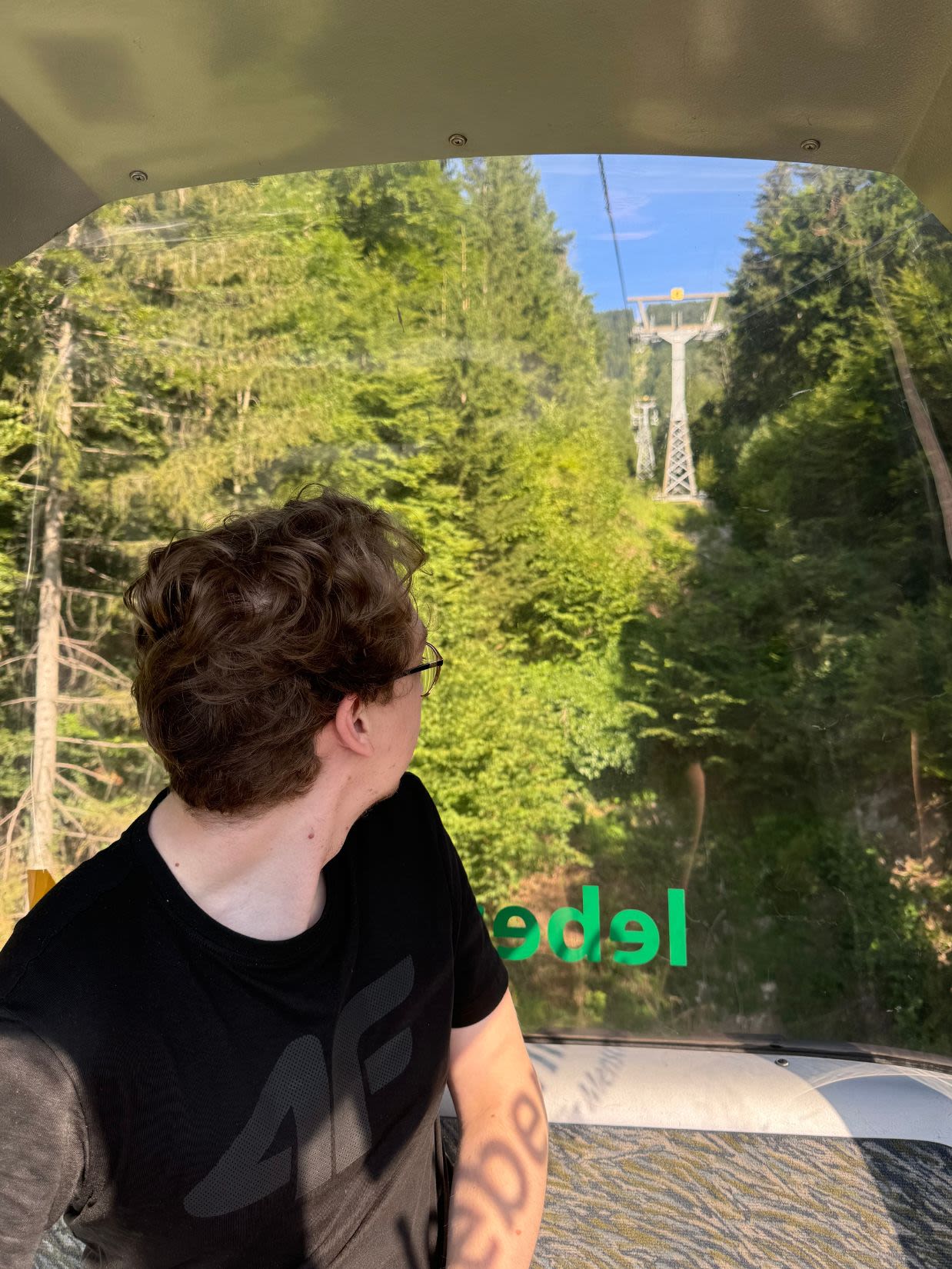Schöcklseilbahn Mountain Station - kolejka na linowa na Schöckl. Mężczyzna siedzi w wagonie i patrzy na zza okno. Zza oknem jest wytyczona trasa na kolejkę i dużo lasu.