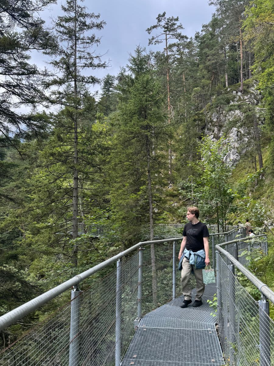 Mężczyzna stoi na metalowej kładce w wąwozie Leutascher Geisterklamm. Wokół rosną wysokie iglaste drzewa.