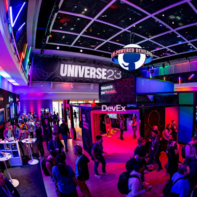 Conference walkway with neon lights on the walls and sign "UNIVERSE23" with a GitHub logo hanging from the ceiling