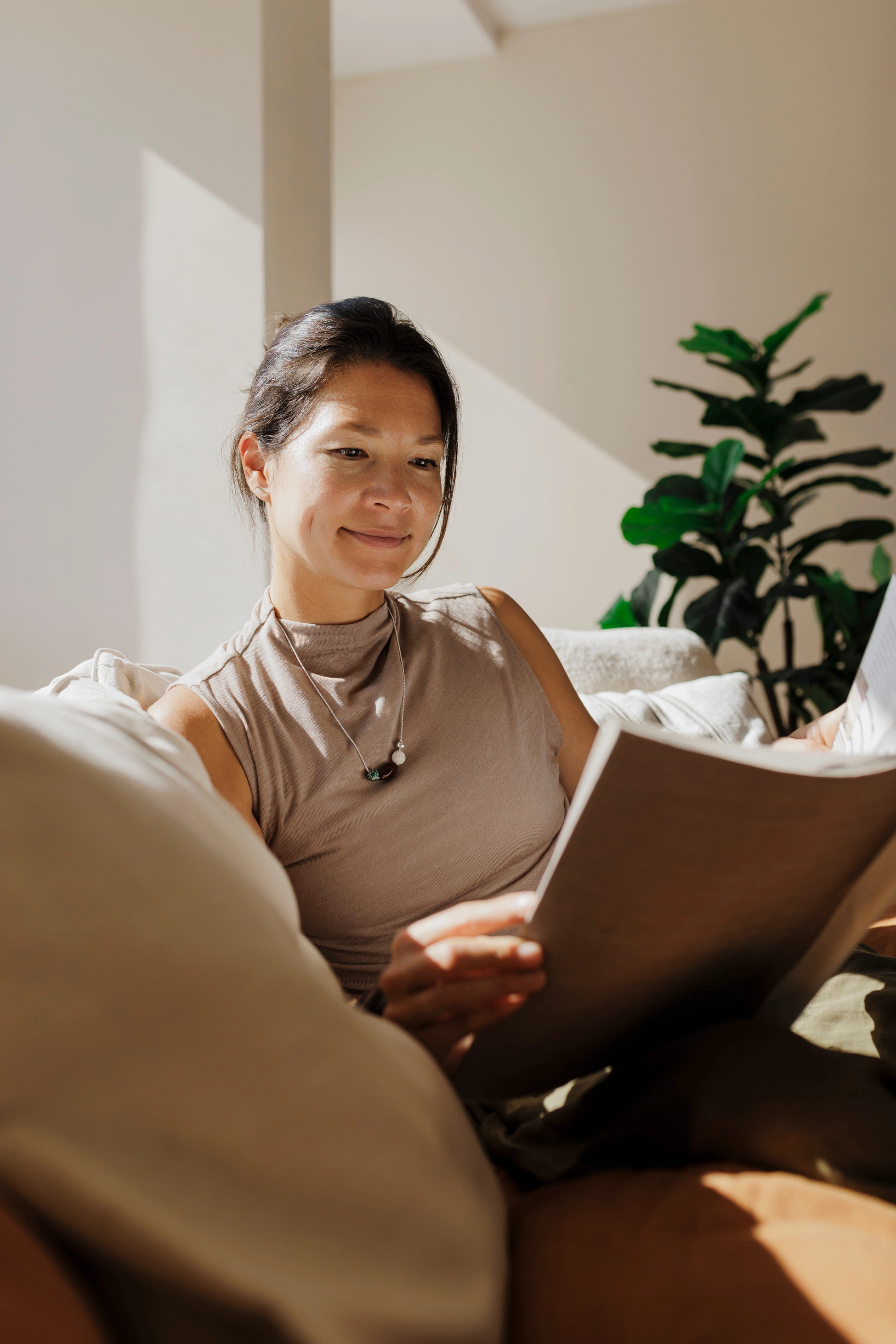 Eine Frau genießt einen ruhigen Moment auf einem bequemen Sofa und liest im warmen Sonnenlicht ein Magazin.
