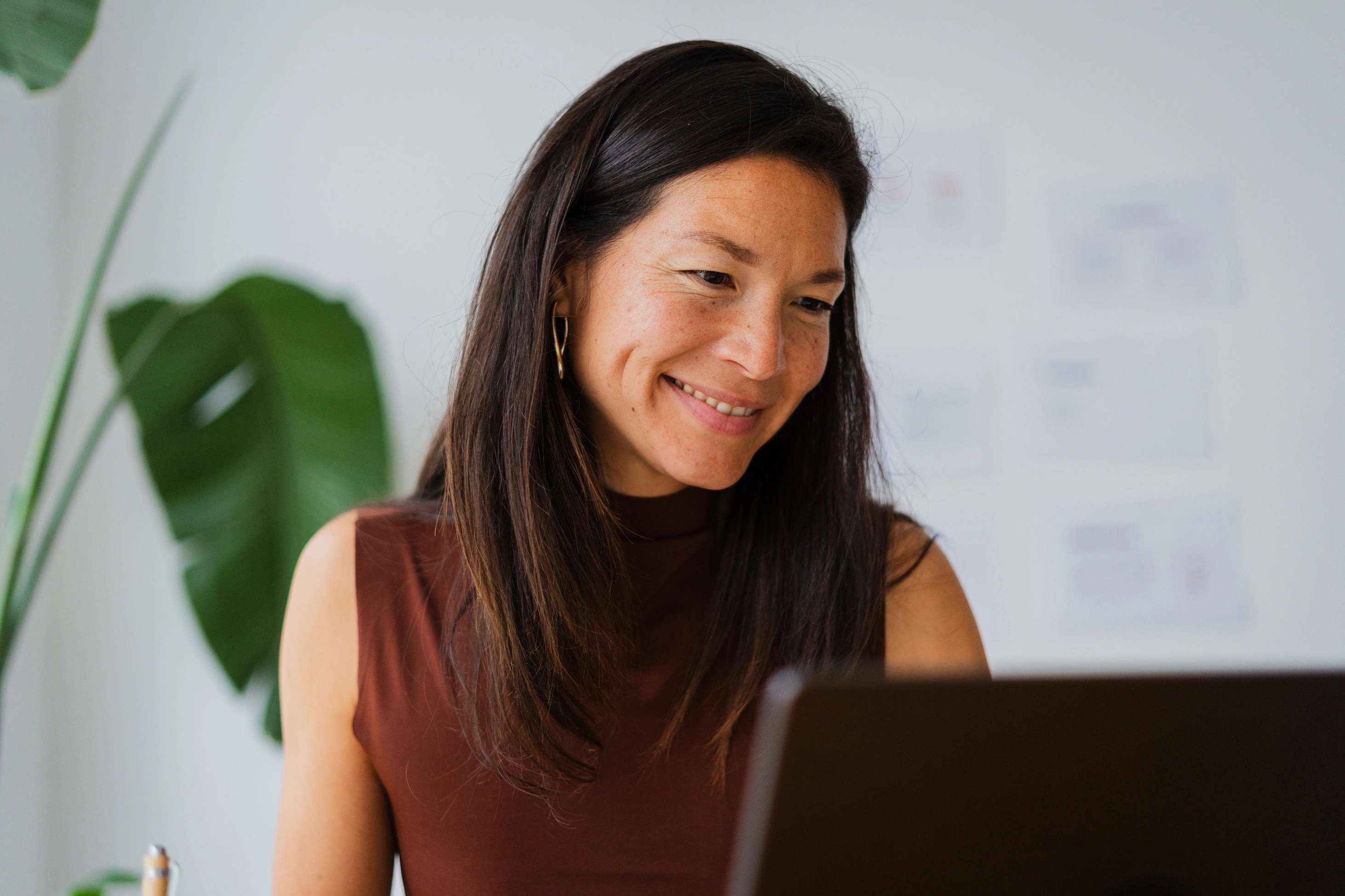 Porträt einer brünetten Frau, die drinnen konzentriert am Laptop arbeitet.