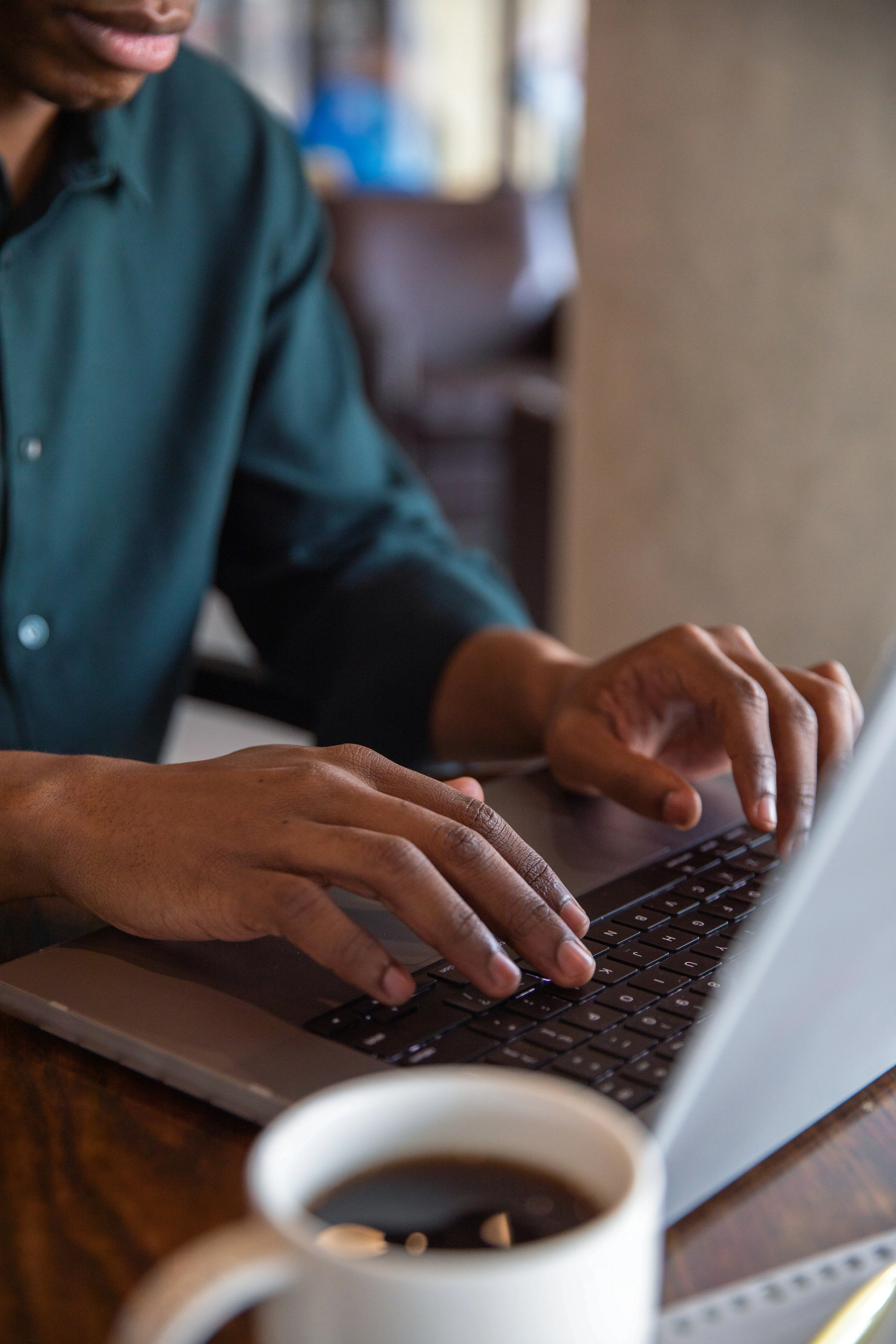 Ein Unternehmer arbeitet in einem Café an seinem Laptop. Er tippt auf der Tastatur, neben ihm steht eine Kaffeetasse auf dem Tisch.
