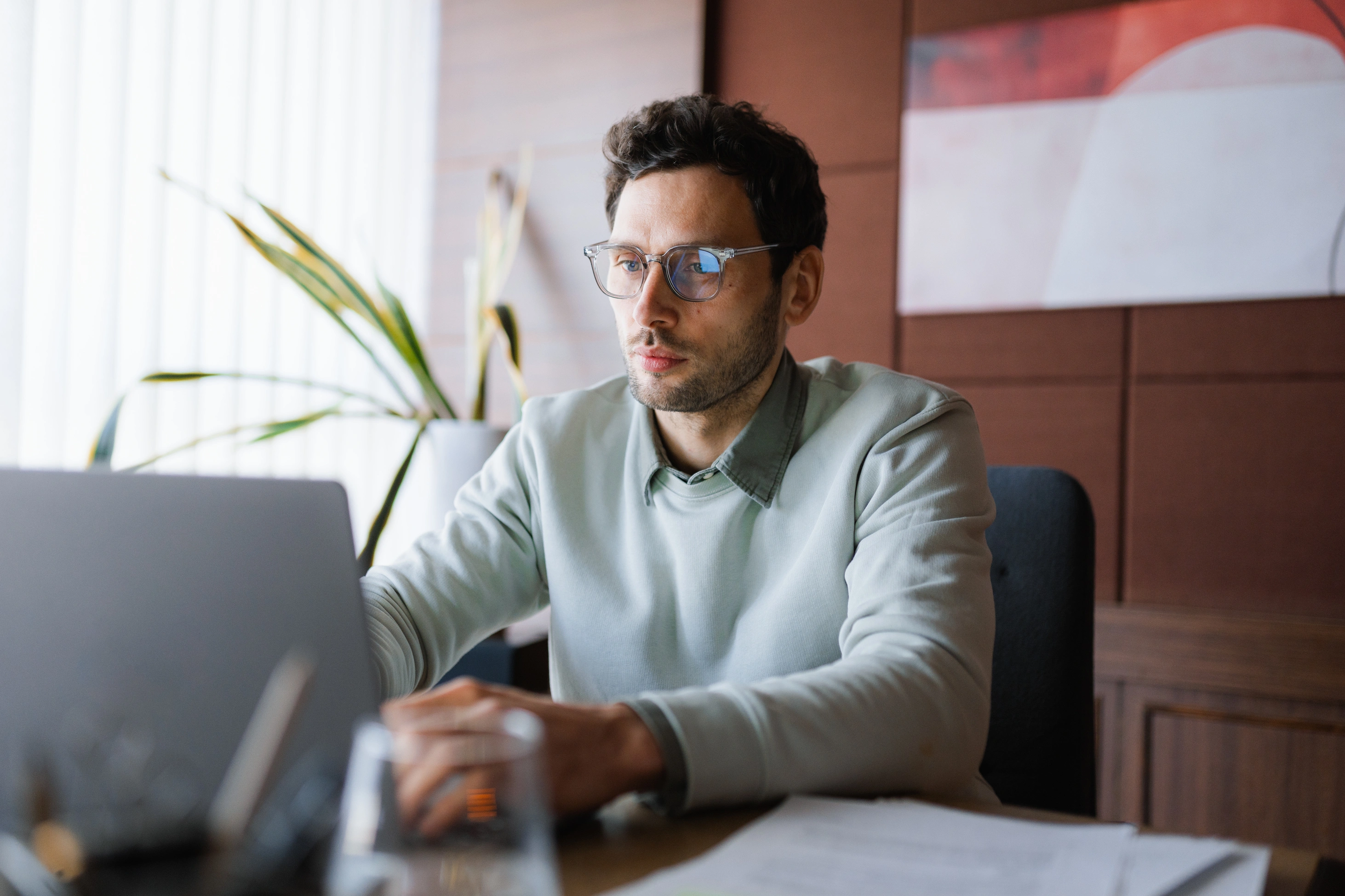 Ein Mann mit Brille sitzt an einem Tisch in einem stilvoll eingerichteten Raum und arbeitet an seinem Laptop.