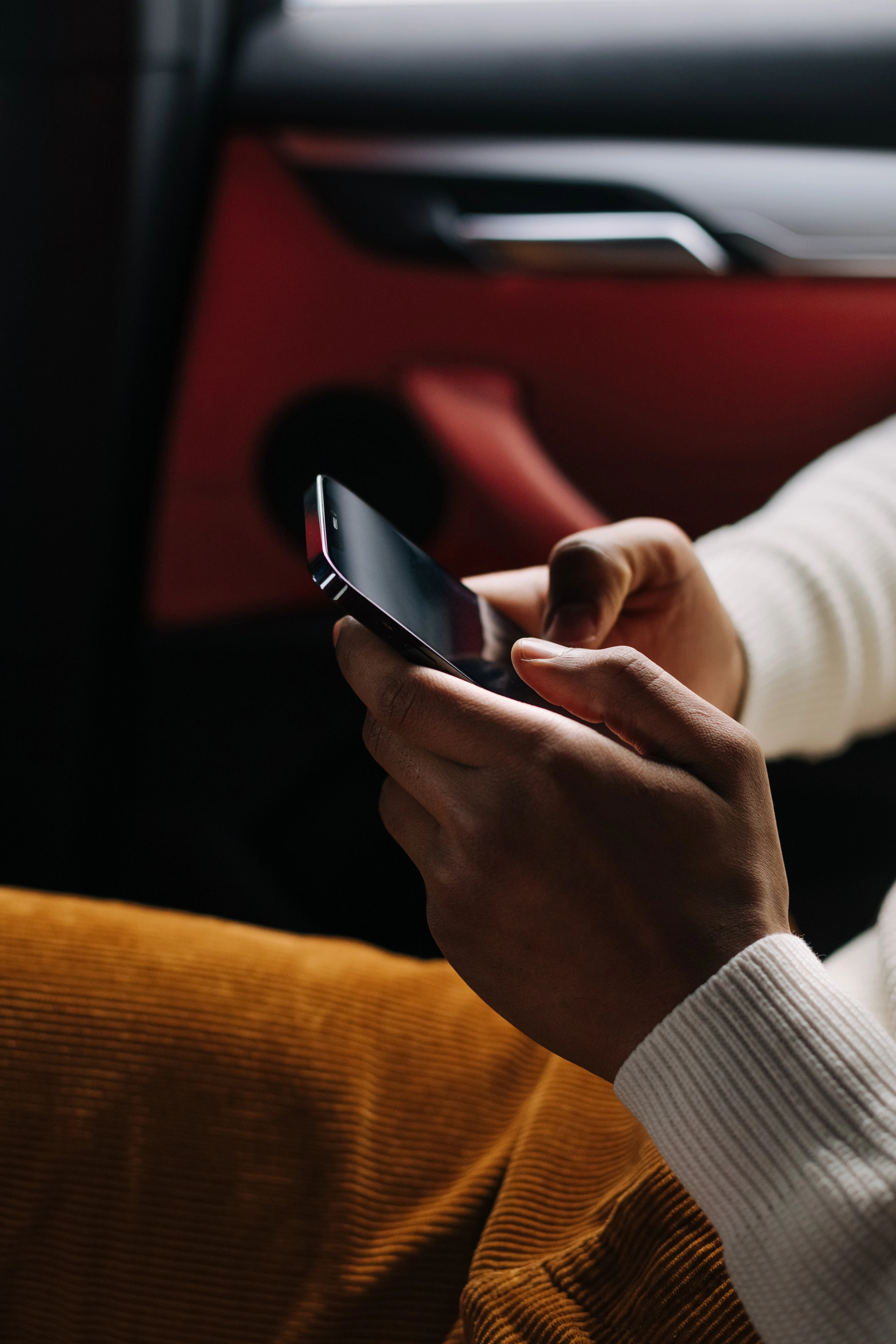 Nahaufnahme eines unkenntlichen jungen Mannes, der auf dem Rücksitz eines Autos sitzt und Nachrichten auf seinem Smartphone schreibt.