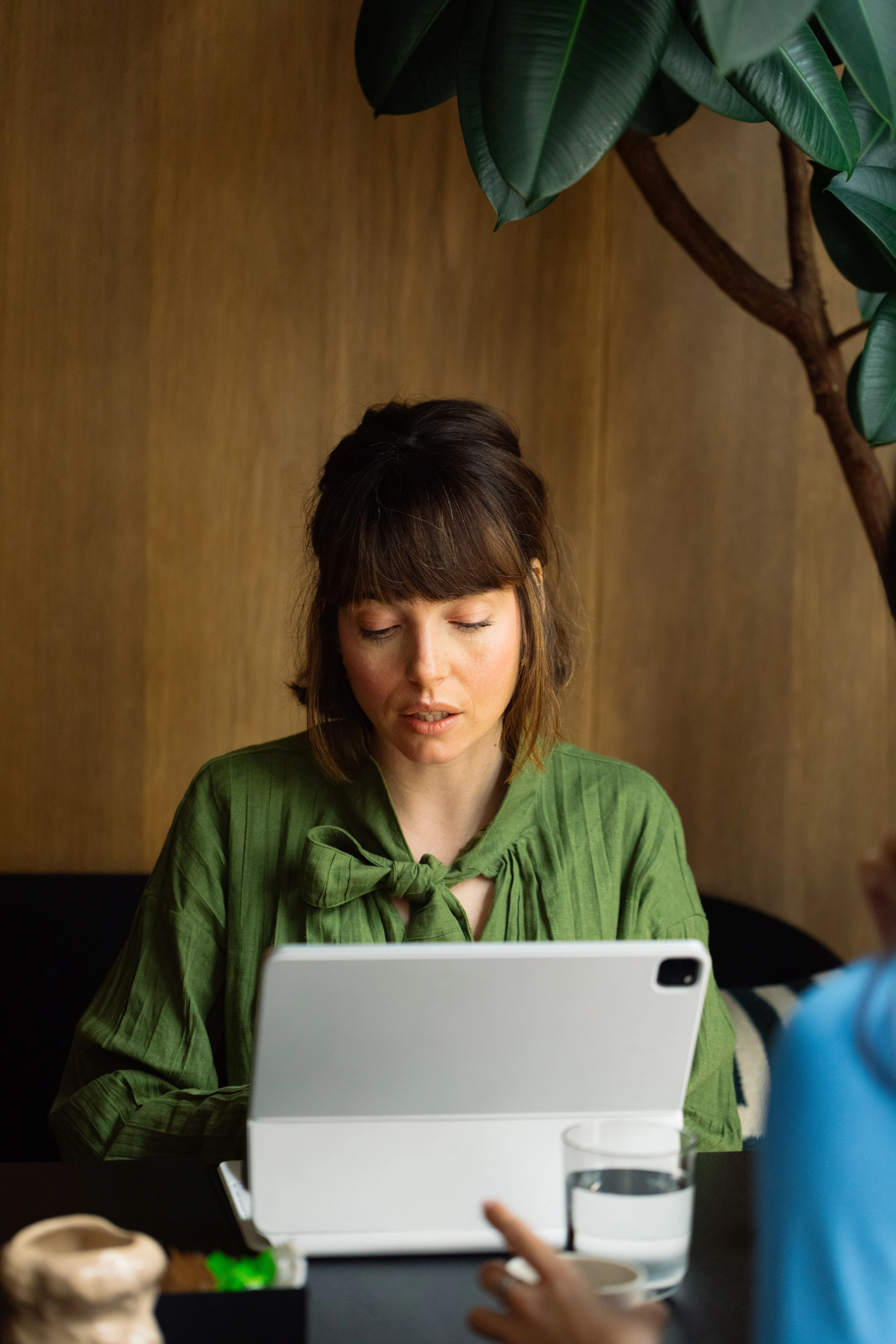 Eine brünette Frau sitzt bei einem Geschäftstermin in einem Café und tippt auf einem Tablet.