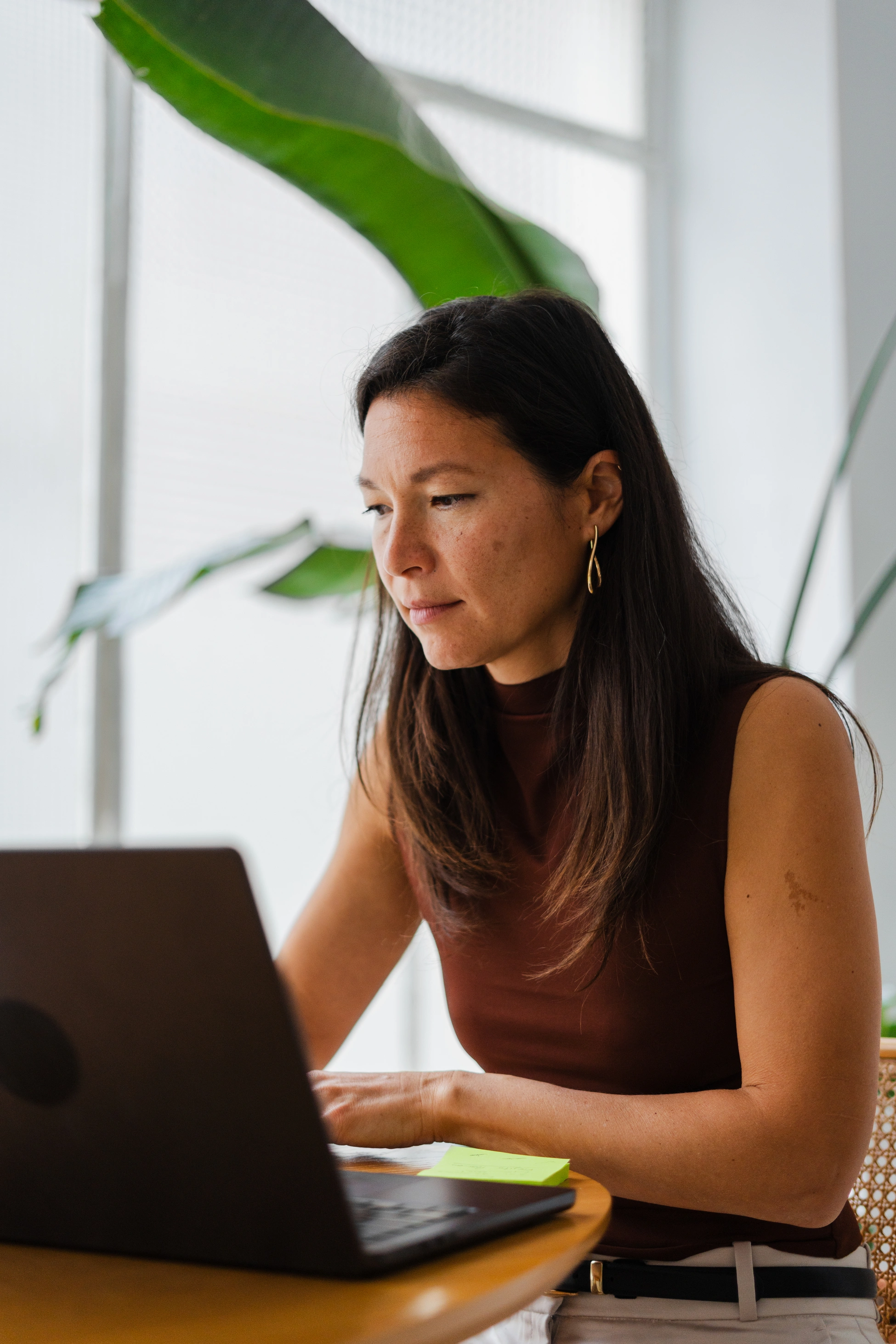 Eine brünette Frau arbeitet drinnen konzentriert am Laptop.