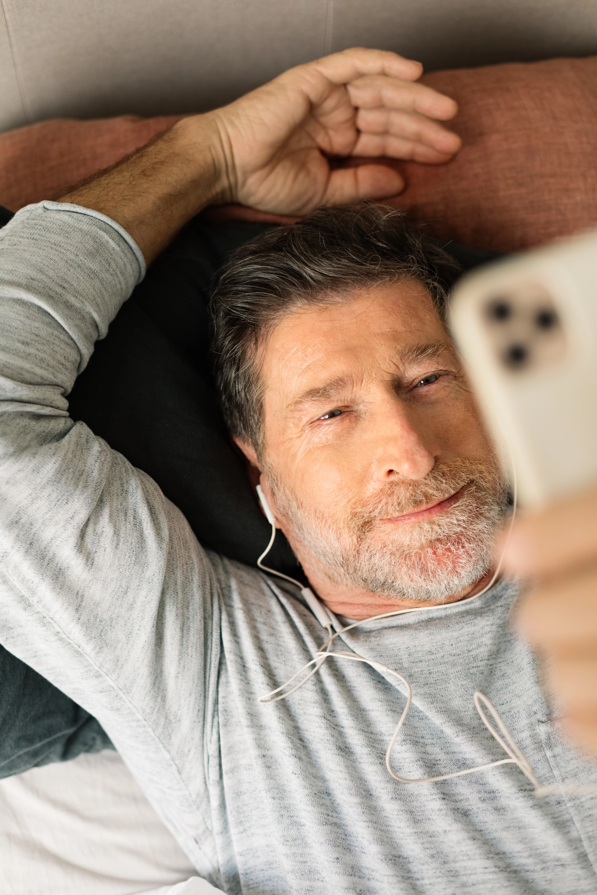 Ein älterer Mann liegt auf dem Sofa und führt über sein Smartphone einen Videoanruf.