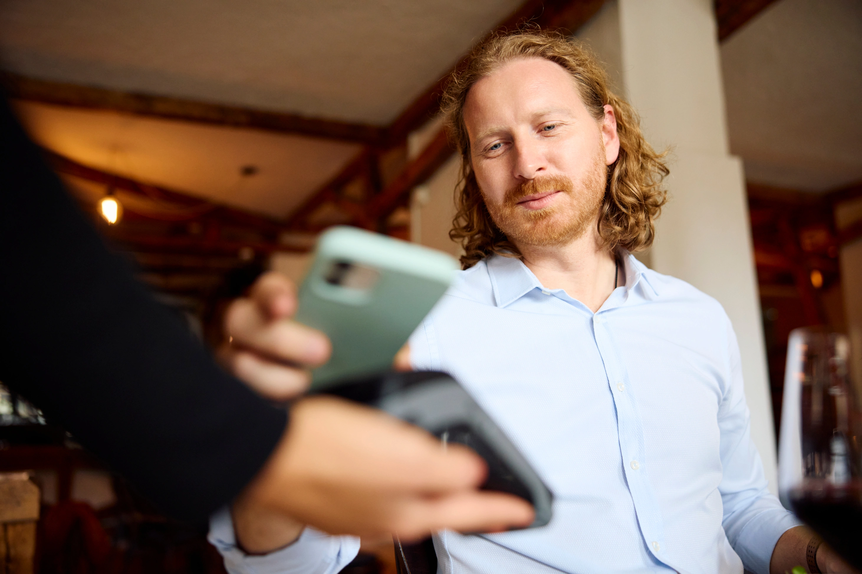 Ein lächelnder Mann im Hemd bezahlt die Rechnung kontaktlos mit seinem Smartphone.