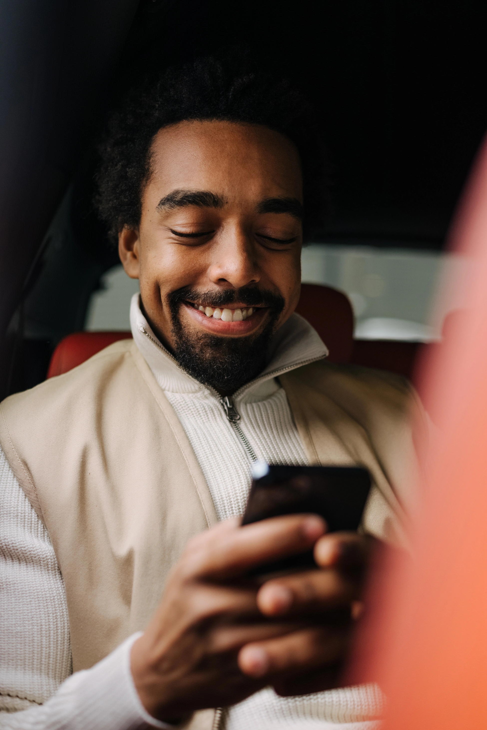 Porträt eines jungen Mannes, der auf dem Rücksitz eines Autos sitzt und Nachrichten auf seinem Smartphone schreibt.