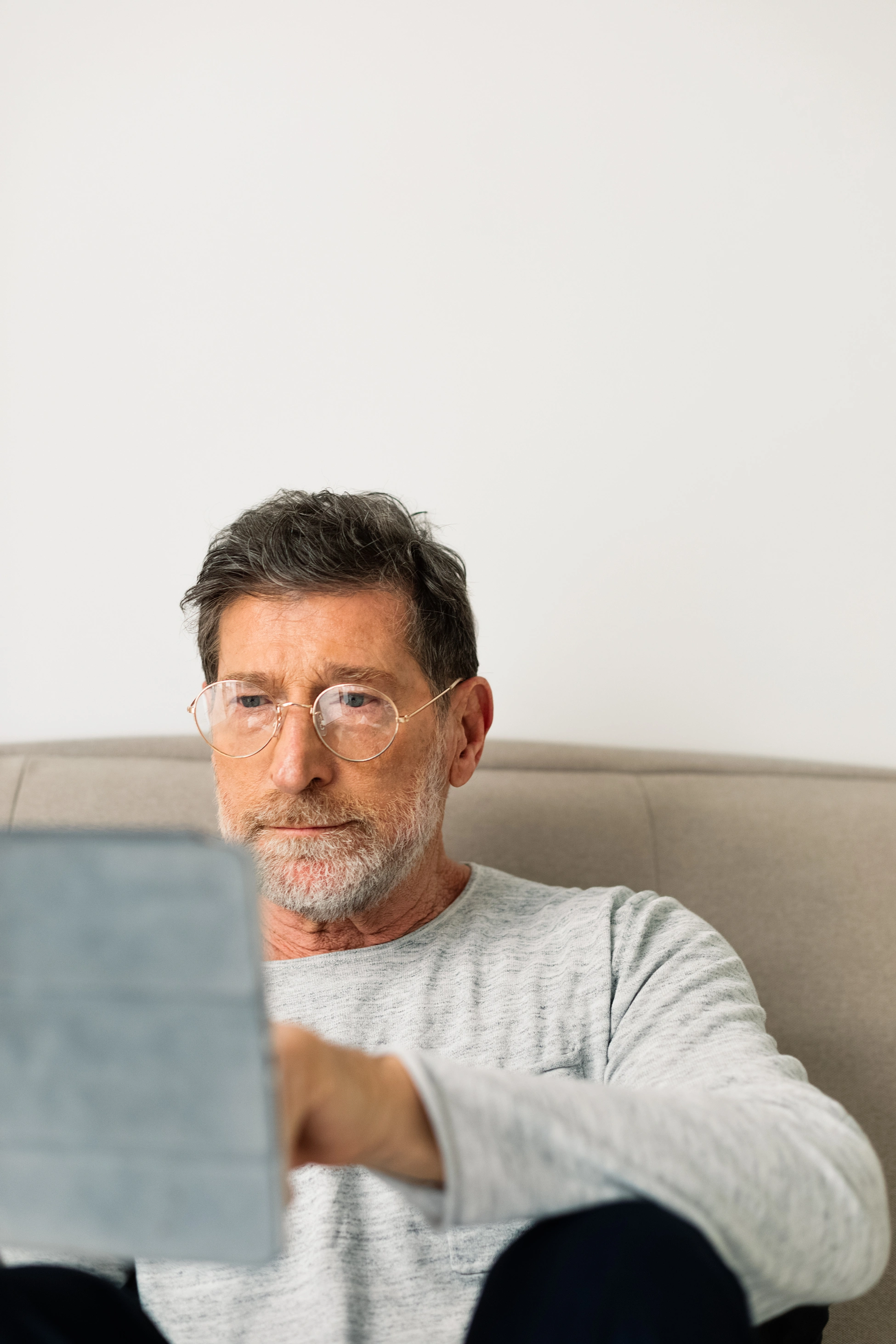 Porträt eines älteren Mannes mit Brille, der auf dem Sofa sitzt und ein Tablet nutzt.