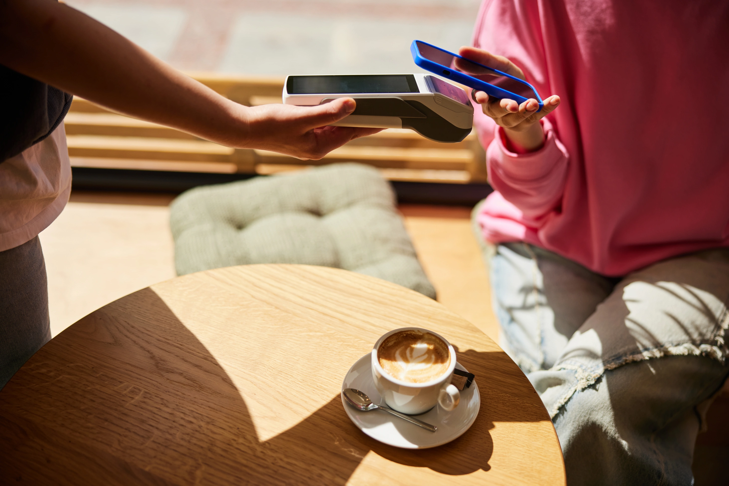 Eine unkenntliche Frau genießt einen Latte macchiato und bezahlt kontaktlos mit ihrem Smartphone.