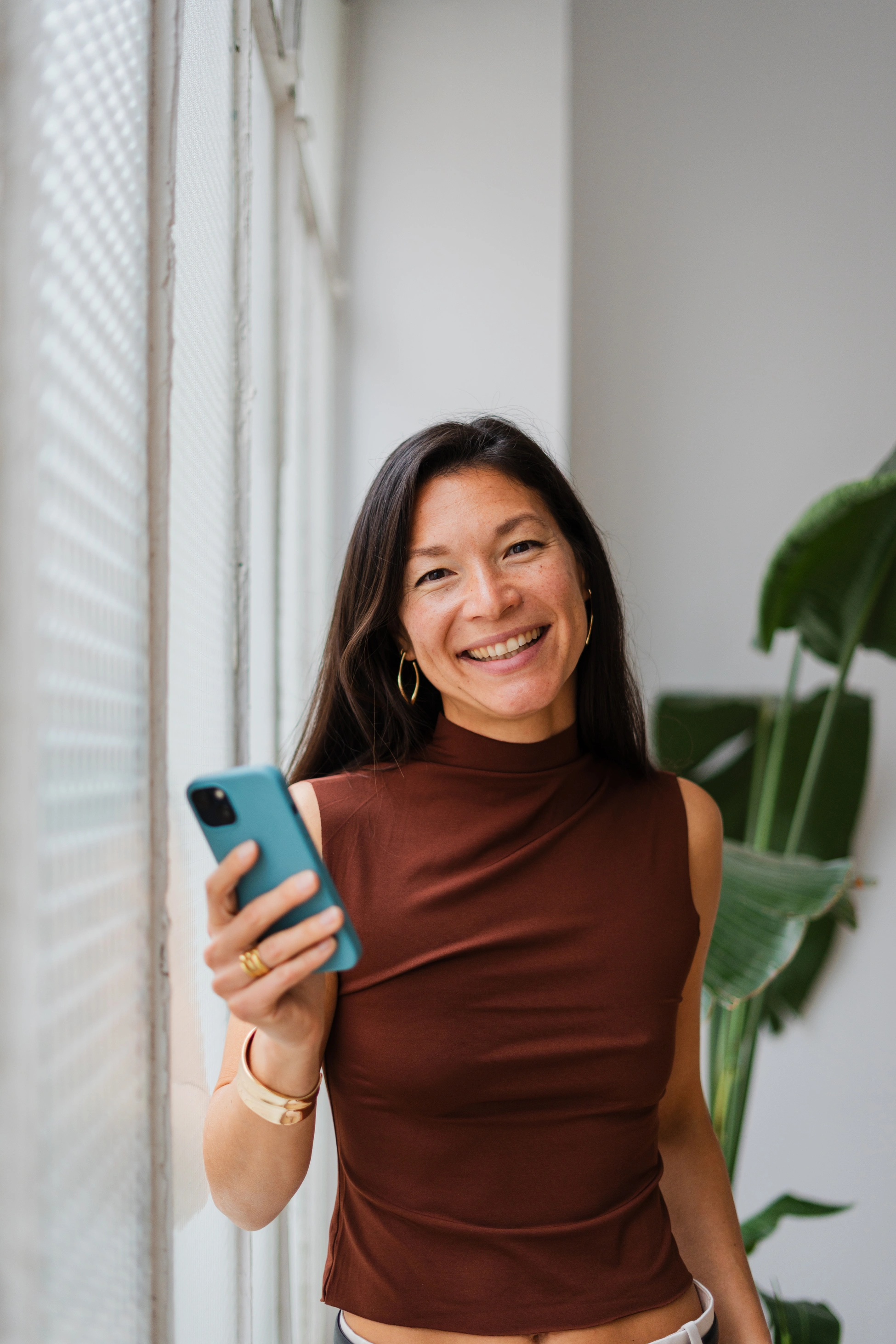 Nahaufnahme einer lächelnden Geschäftsfrau, die in die Kamera blickt und ihr Smartphone in der Hand hält.