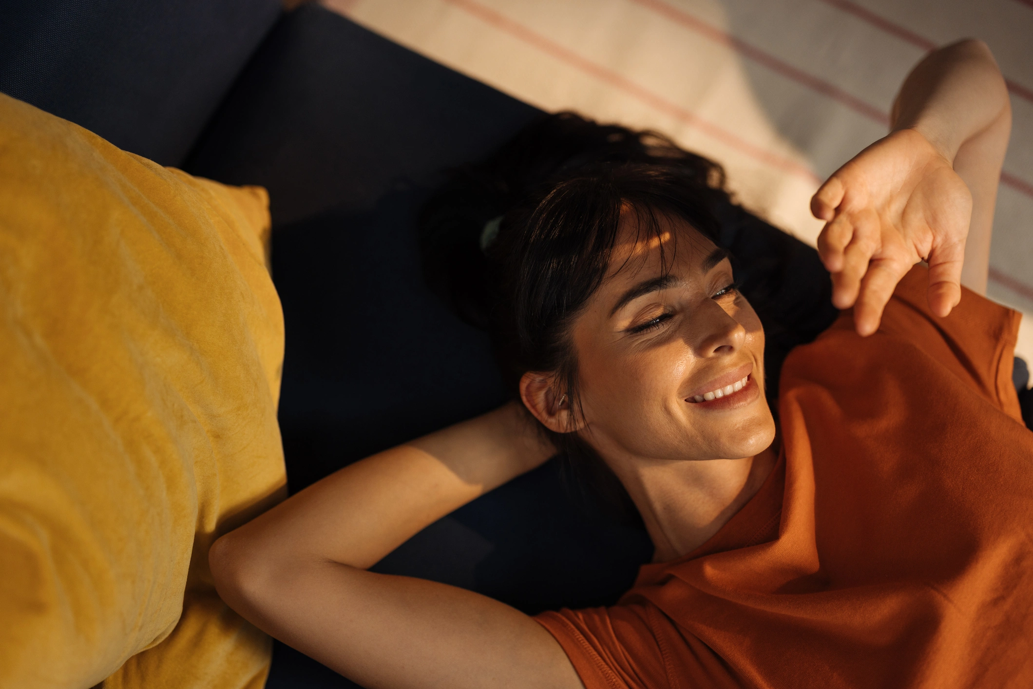 Entspannte Frau, die zu Hause auf der Couch liegt und warmes Licht und gemütliche Atmosphäre genießt.