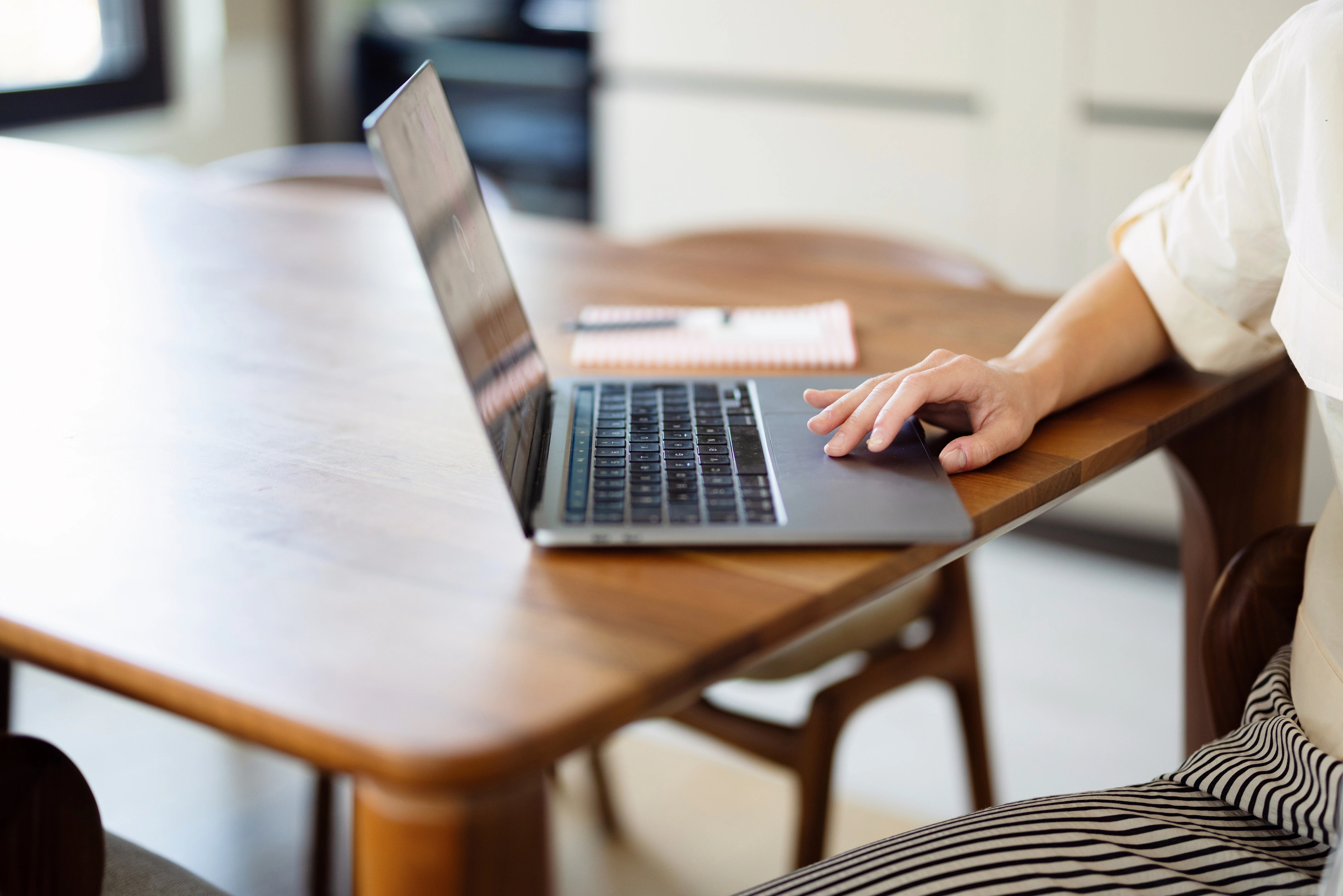 Eine Person arbeitet konzentriert an einem Holztisch im Homeoffice am Laptop, daneben liegt ein Notizbuch.