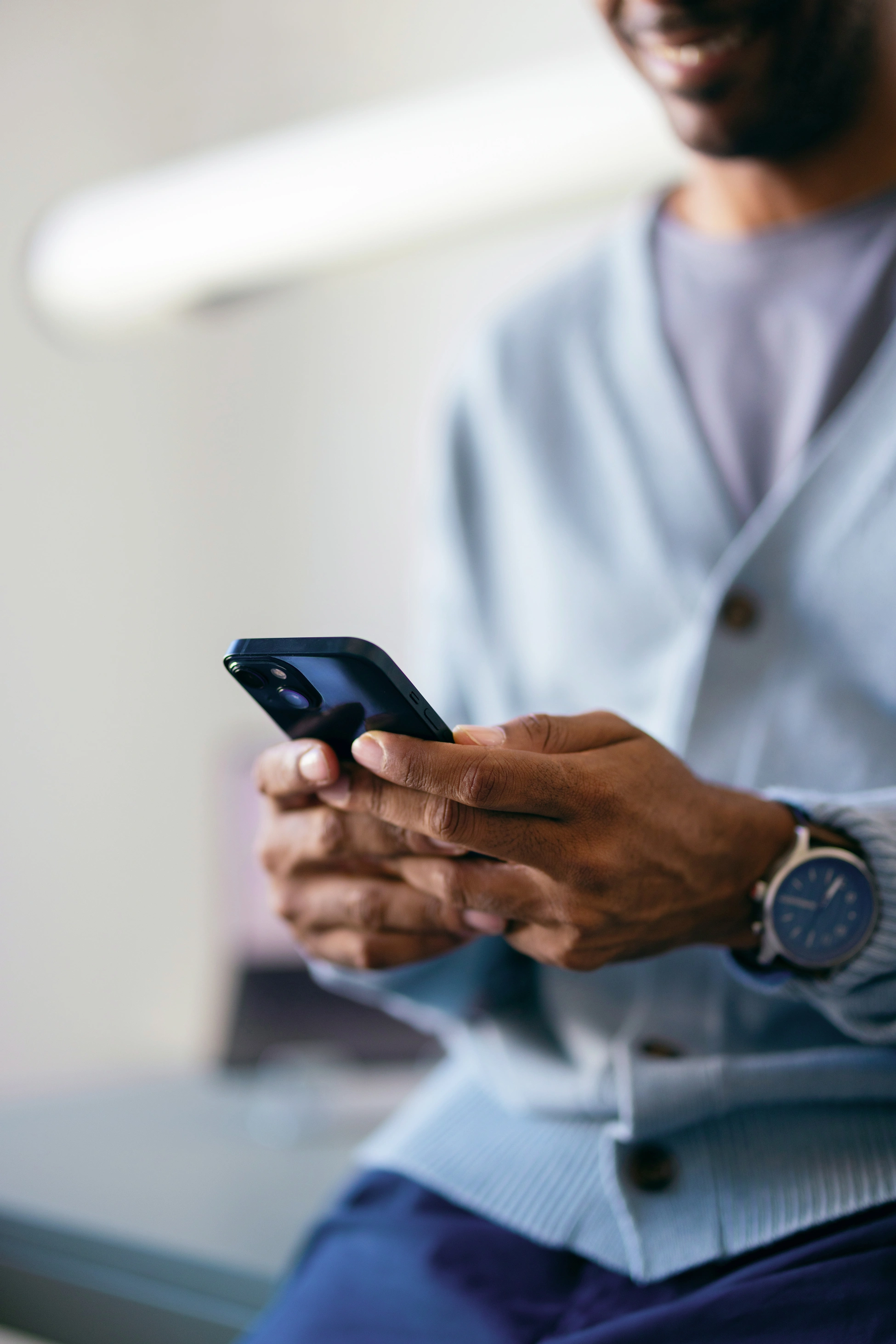 Ein Mann schreibt bei der Arbeit lächelnd Nachrichten auf seinem Smartphone.
