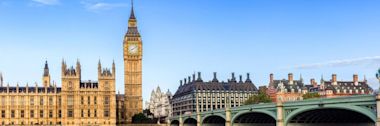 Big Ben and Houses of Parliament along River Thames with Westminster Bridge in foreground under clear blue London sky
