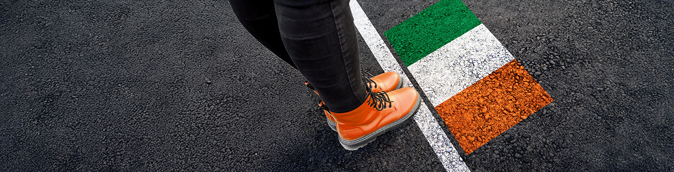 A person wearing orange boots standing on asphalt next to flag of Ireland painted on it