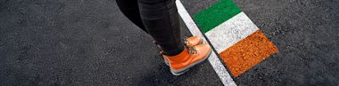 A person wearing orange boots standing on asphalt next to flag of Ireland painted on it