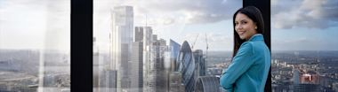 A attractive business woman in a corporate outfit looks out of a skyscraper at the city skyline of London, England