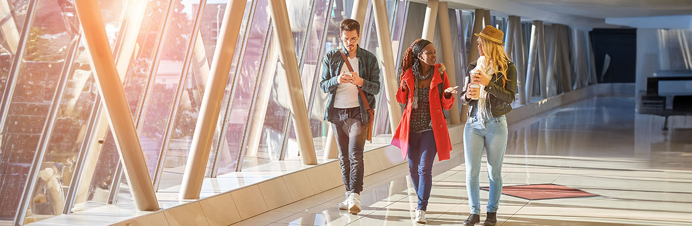 Three students of mixed race walking with coffee and cellphone in the school hallway