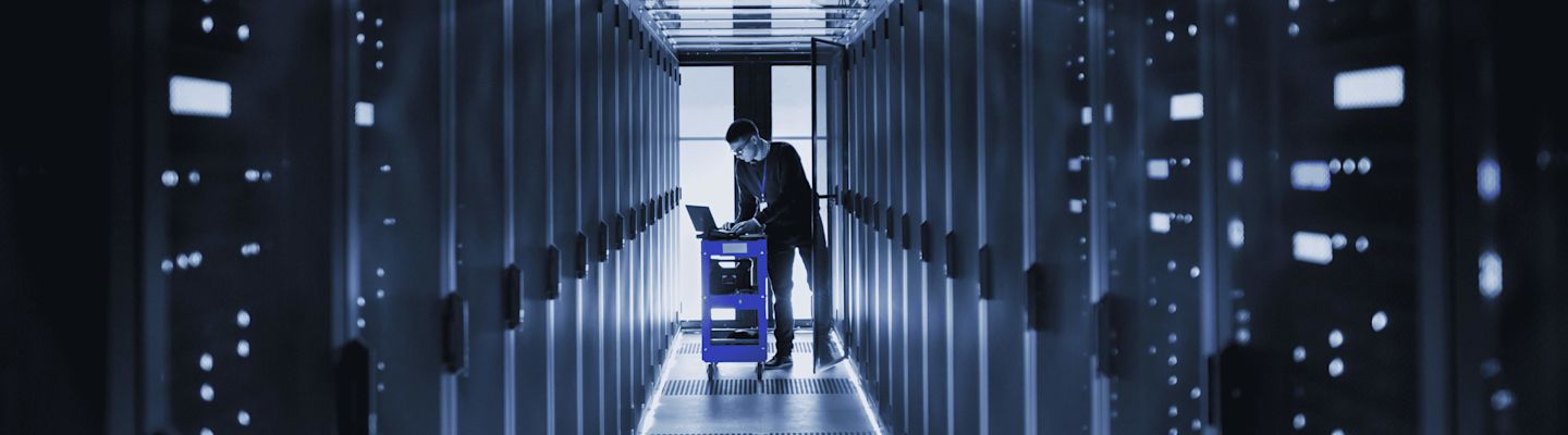A student in blue t-shirt, working on his laptop with a headphone.