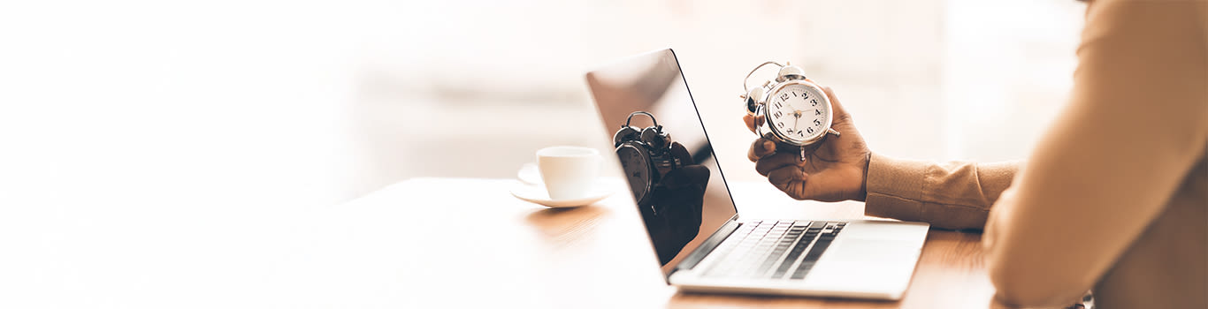 Time passing concept, a person sits in front of a laptop, looking at an analog clock
