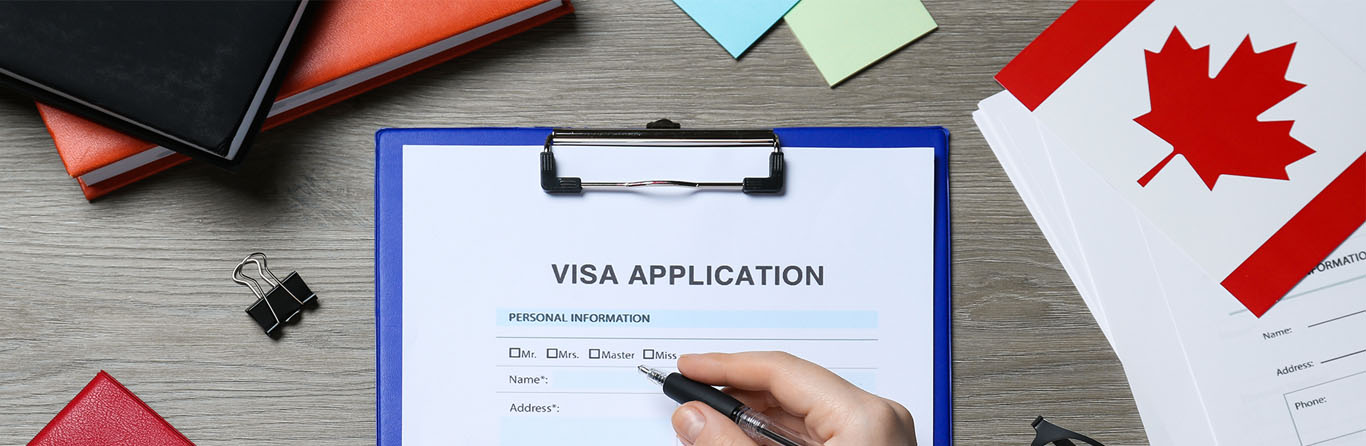 A person filling out a visa application form for Canada at a wooden table, top view