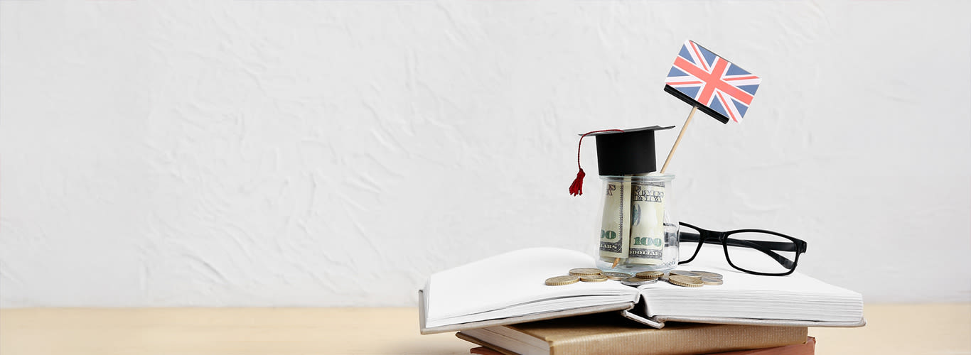 Jar of money with UK flag and books on table near a lightly coloured wall. 