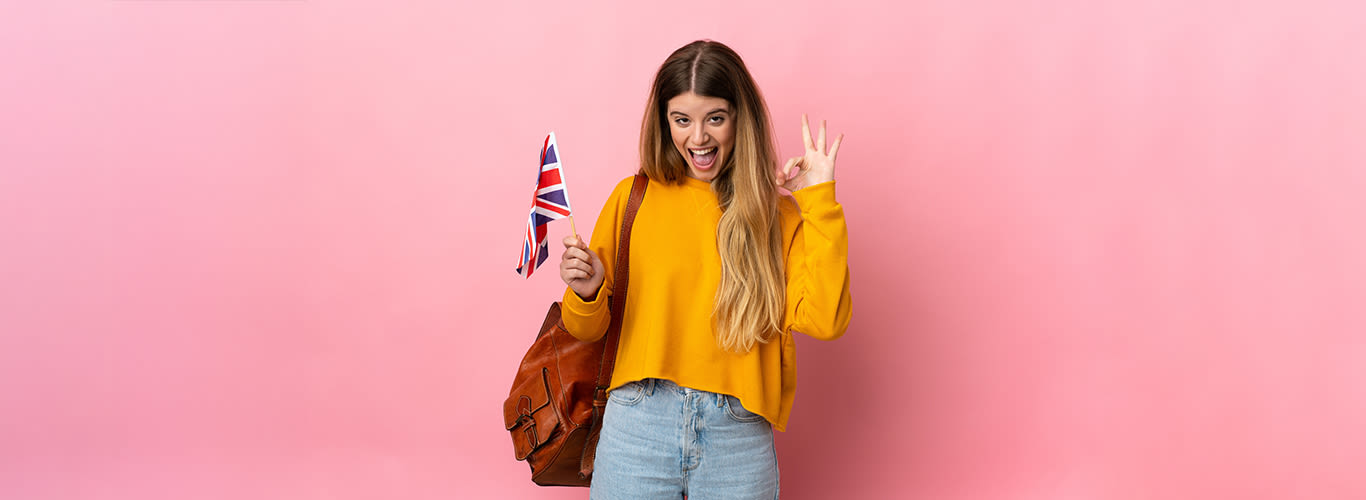 Happy human expressing an OK with their hand and holding a UK flag against a pink background