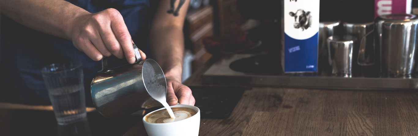 barista pouring latte art in a cup of coffee
