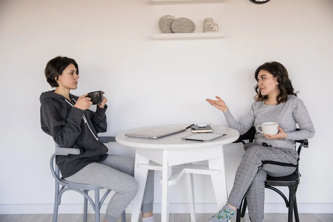 two seated woman speaking to each other over a table in between them