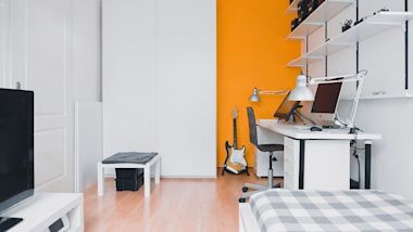 Modern home office with white desk, orange accent wall, electric guitar, and floating shelves in a minimalist room setup