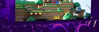  Audience silhouettes watch large screen displaying Mario-style video game level with green platforms, coins, and question blocks