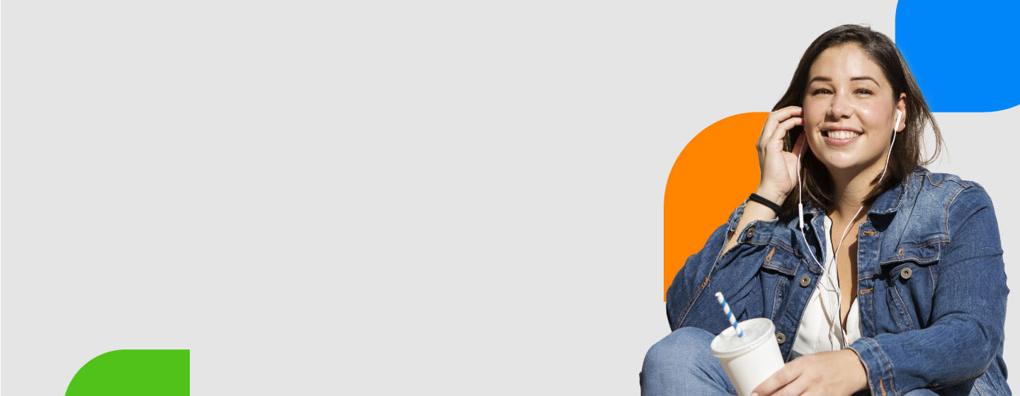 A person in a denim jacket listens to music with earphones while holding a cup, set against a light grey background