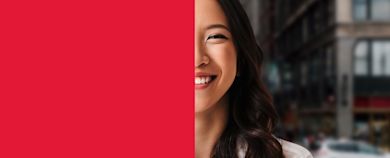 A woman smiling with half of her face visible on a red background. The other half shows a blurred city street in the background.