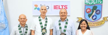 Four people wearing green and white sashes standing in front of IDP IELTS logo.