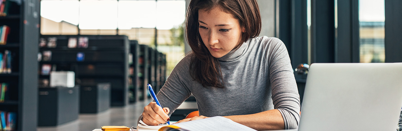 woman writing on book behind a table