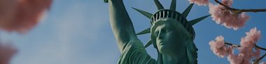 The Statue of Liberty is framed by pink cherry blossom branches against a clear blue sky.