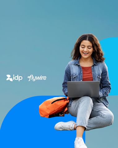 A young woman smiles while using a laptop, sitting cross-legged with an orange backpack. The background is blue with the logos for idp and flywire displayed beside her.