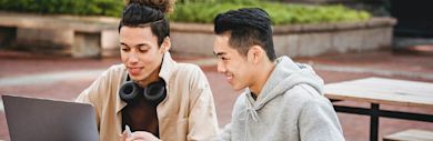 Two students sitting outside looking at a laptop