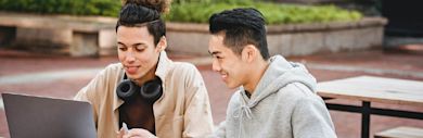 Two students sitting outside looking at a laptop